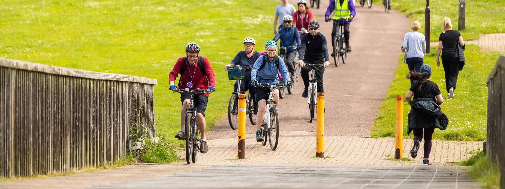 Cyclists crossing a bridge in parkland with a lake beside them