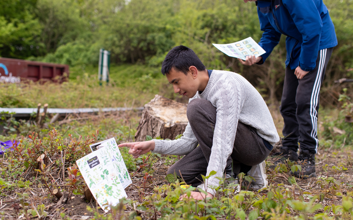 A group stood outside, a teacher giving an explanation to 3 students, one with a clipboard