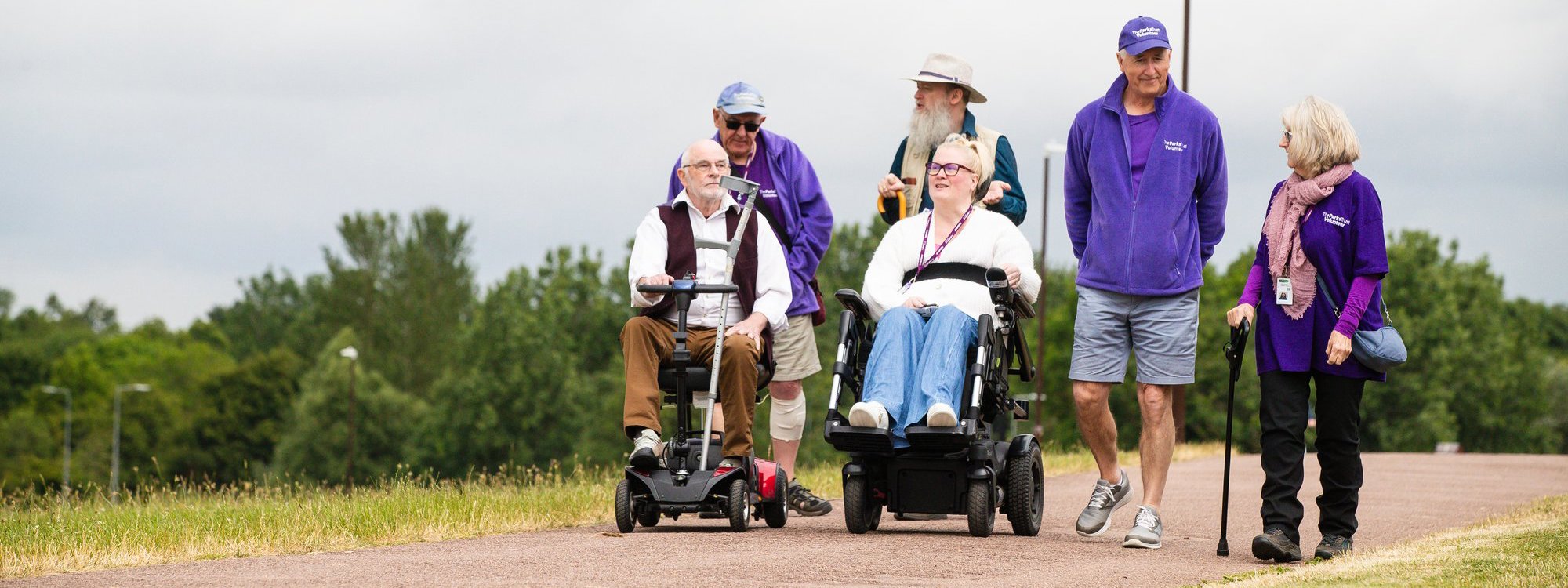 Group of people, two in wheelchairs and one holding on a path in a park