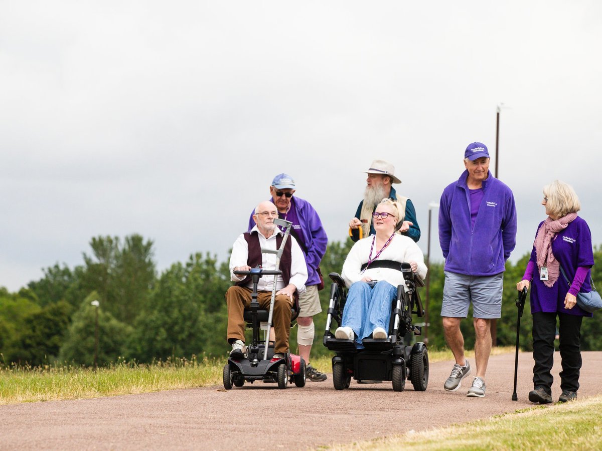Group of people, two in wheelchairs and one holding on a path in a park
