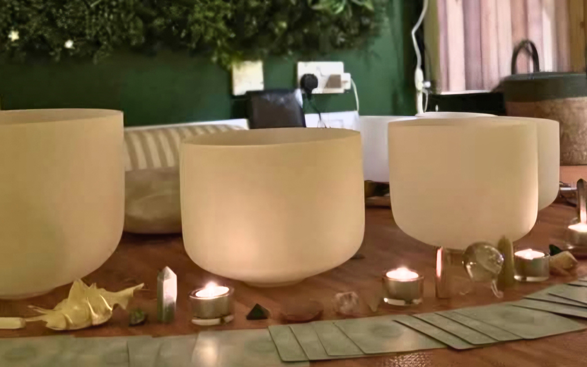 A collection of white singing bowls with glowing candles placed next to them.