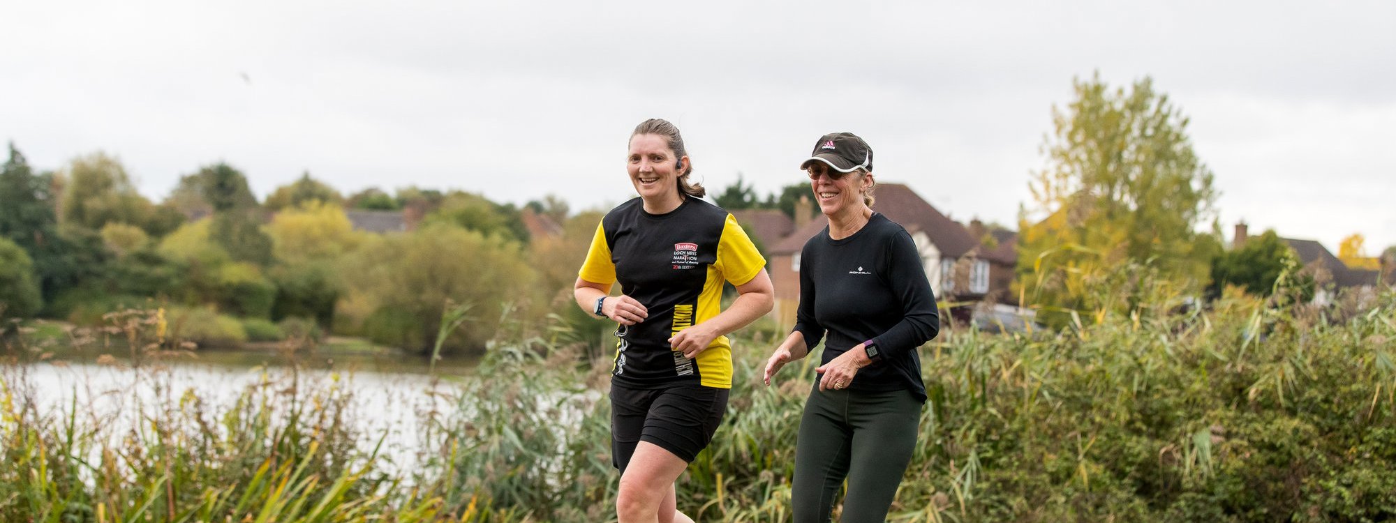 Two smiling female runners with Furzton Lake in the background