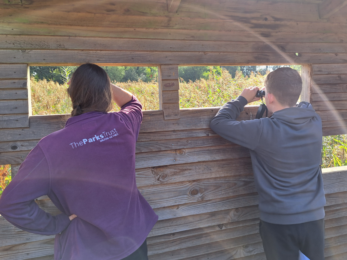 Two teenagers looking out from a bird hide with backs to the camera