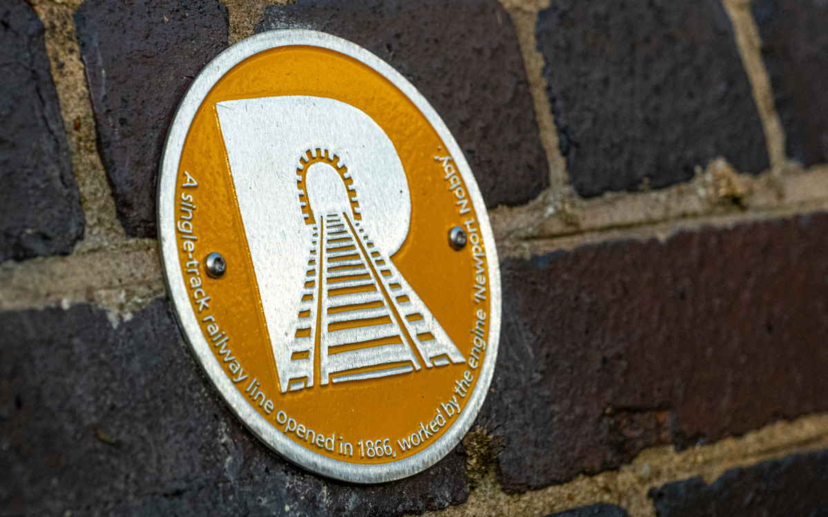 Yellow and silver letter 'R' against a brick wall.