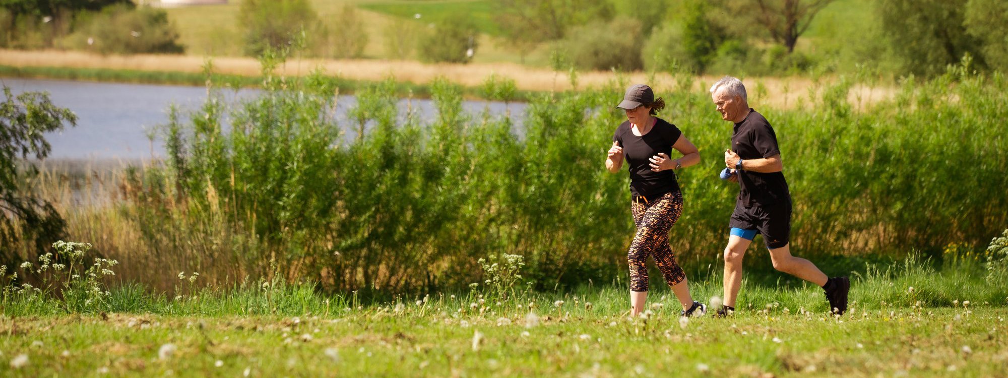 A pair of runners in green parkland with Willen Lake and the Peace Pagoda in the background
