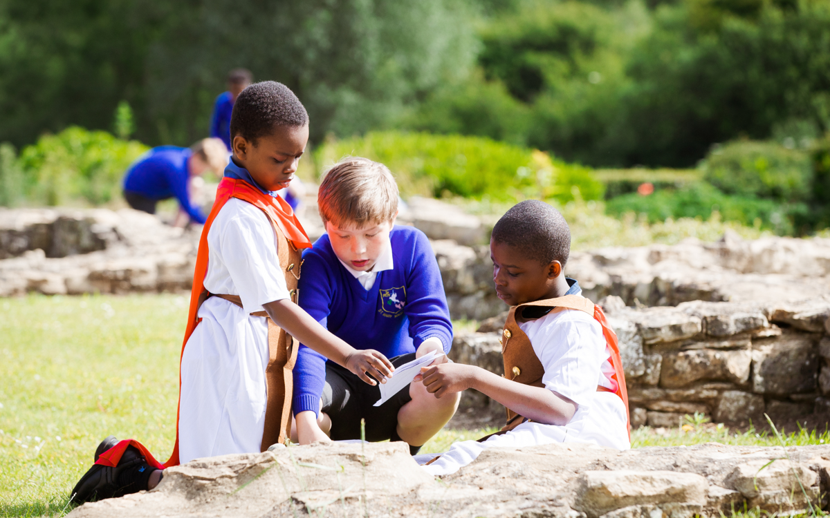 Children wearing Roman costumes studying Roman building remains outdoors in the sunshine