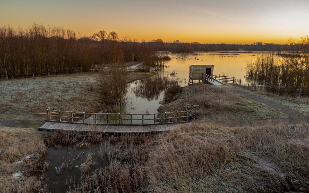 Sunset over boardwalks and bird hide, with lake.