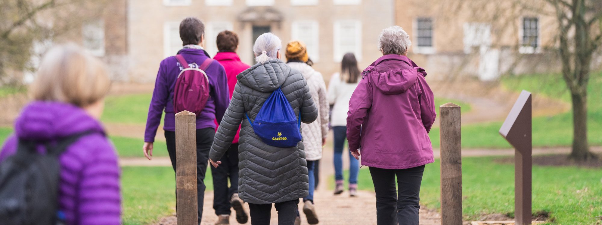 A group of women walking in a parkland scene with a manor house in the background. 