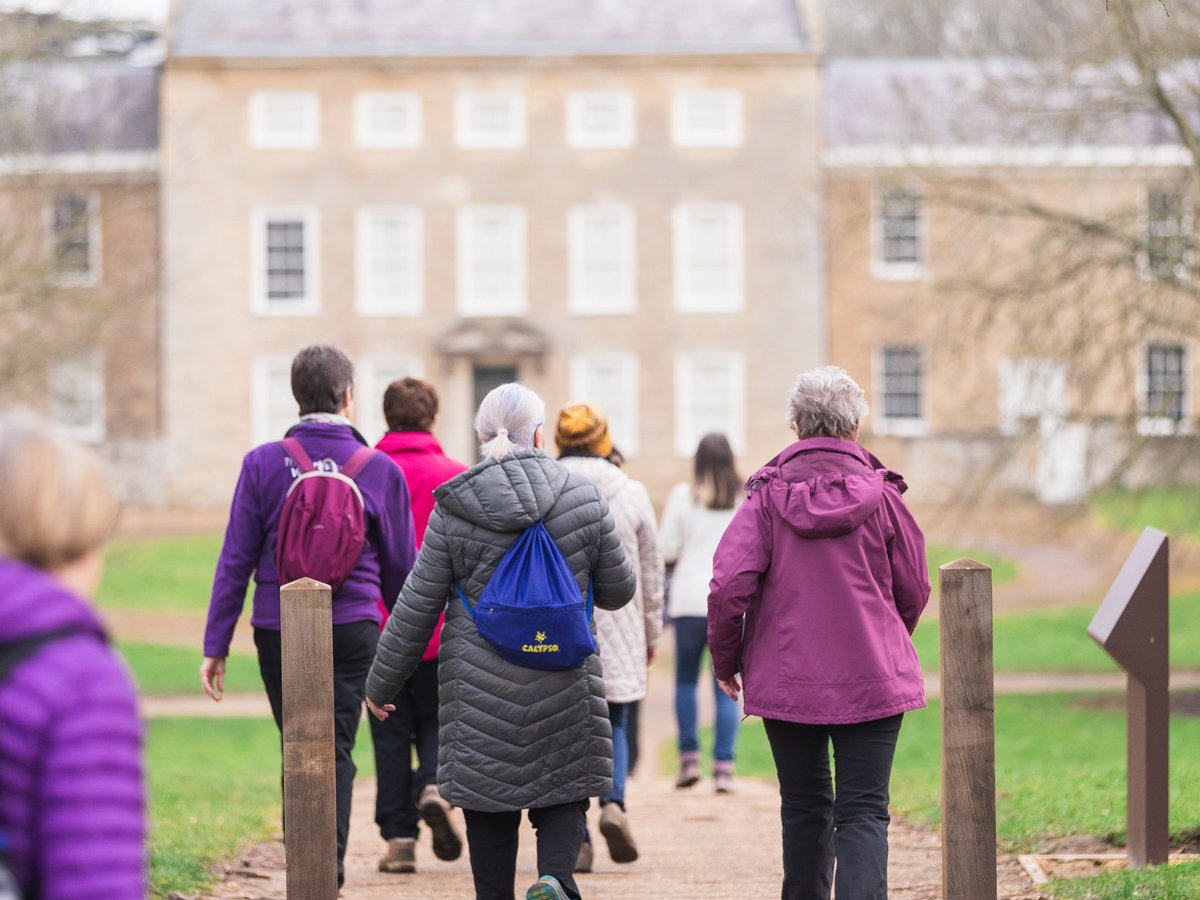 A group of women walking in a parkland scene with a manor house in the background. 