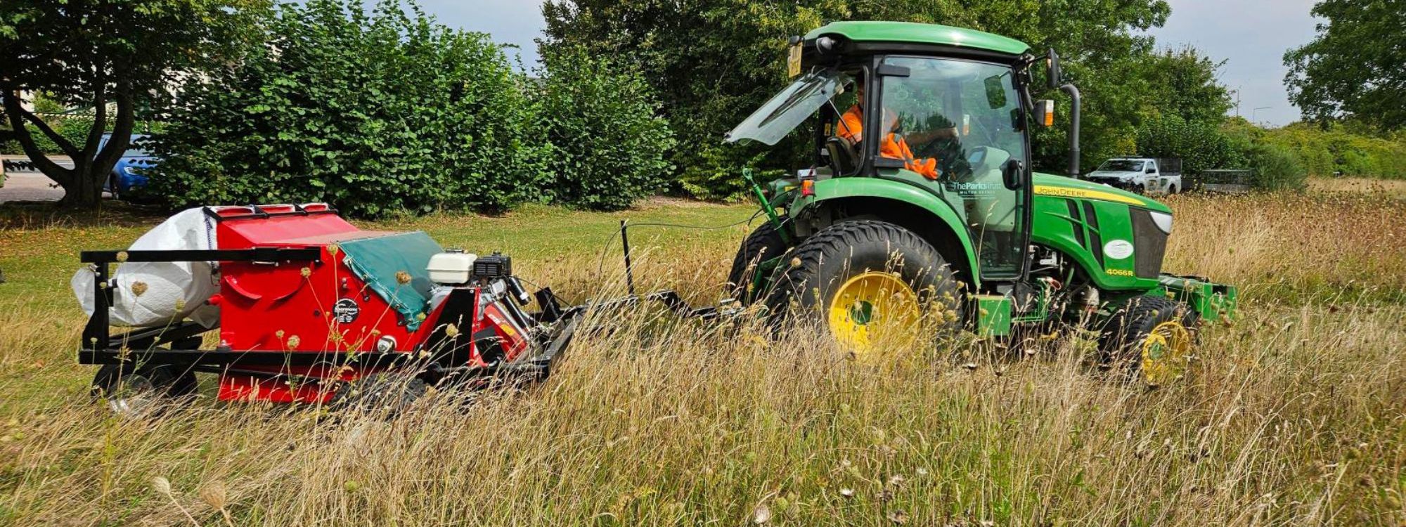 Green tractor pulling seed harvester in meadow