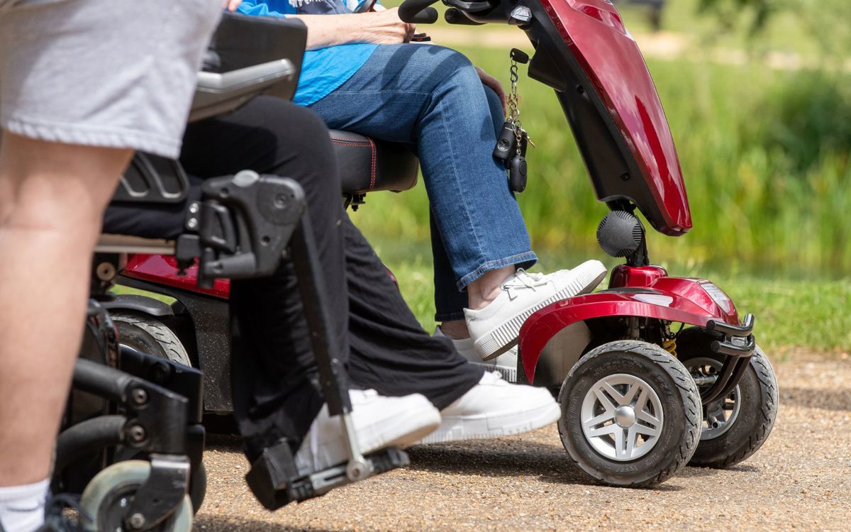 A mobility scooter and a wheelchair in parkland