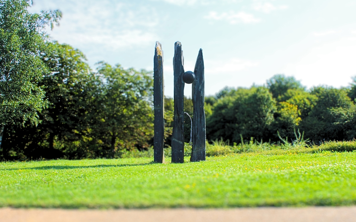 this stone structure has 3  varying vertical rectangular poles however between the 2nd a 3rd pole a large stone ball has been merged into the gap between the poles 