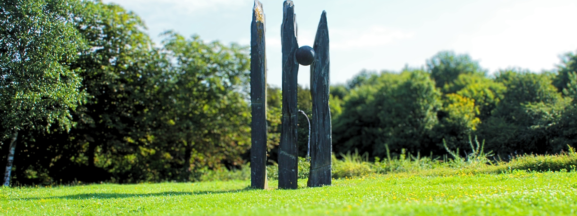 this stone structure has 3 varying vertical rectangular poles however between the 2nd a 3rd pole a large stone ball has been merged into the gap between the poles
