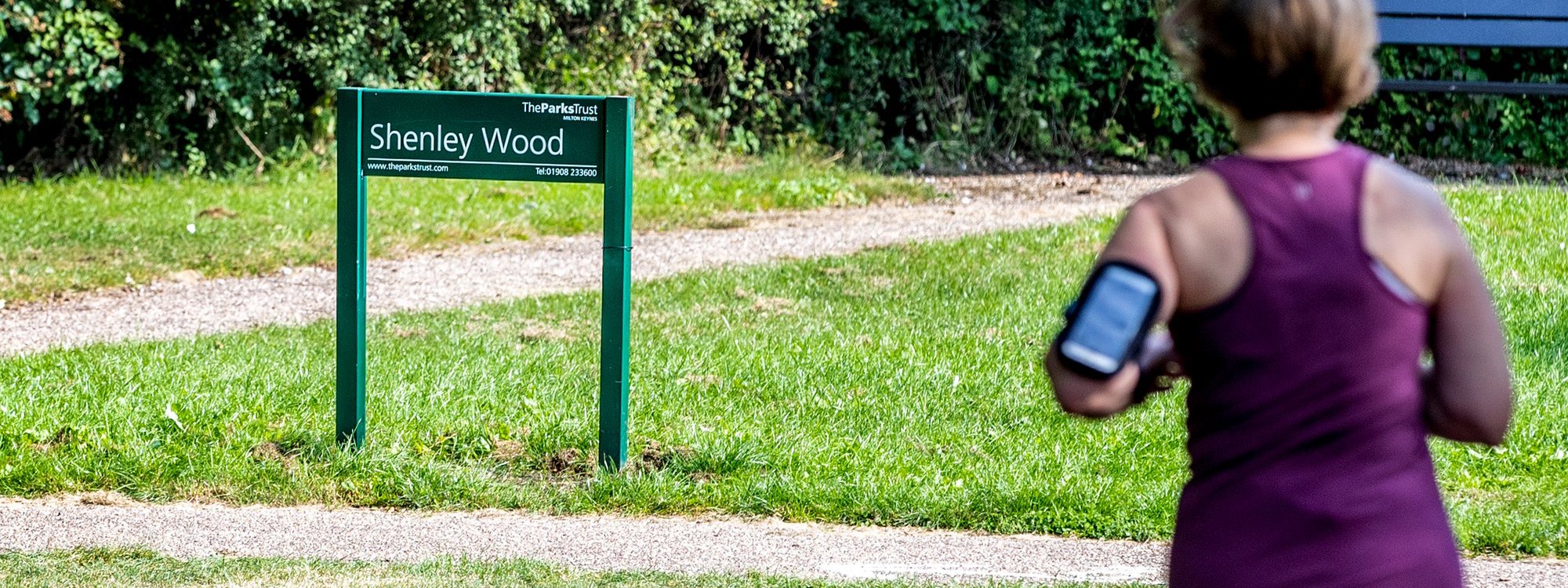 A solo female runner with Shenley Wood in the background
