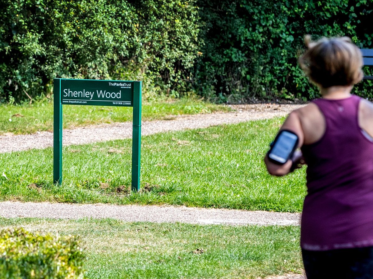 A solo female runner with Shenley Wood in the background