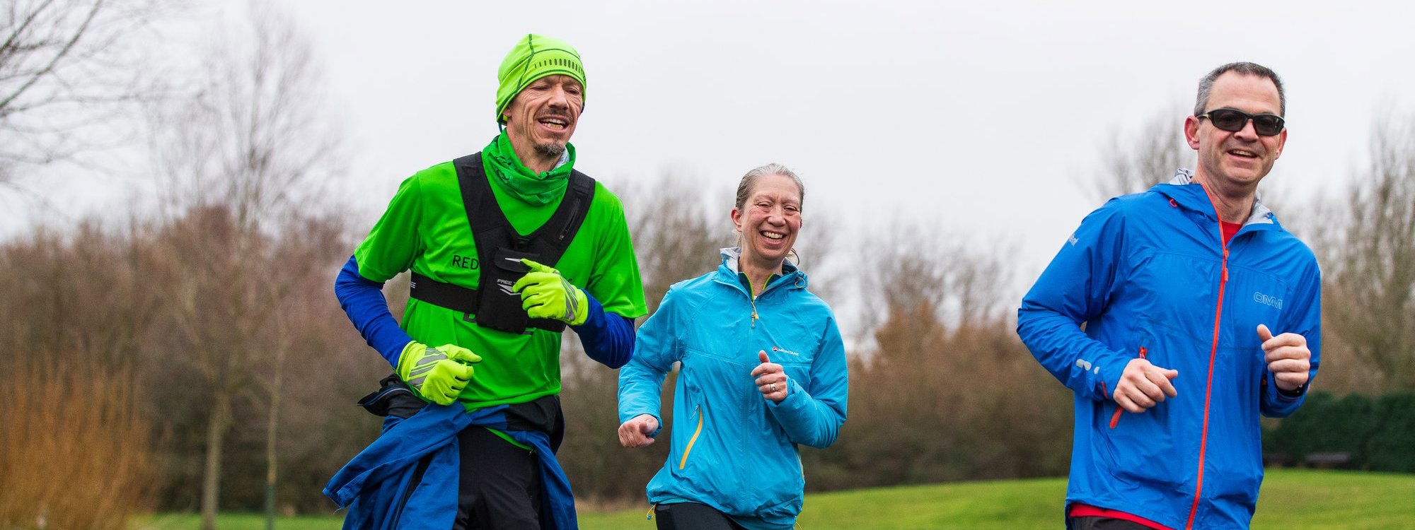 Two male and a female runner in a parkland area