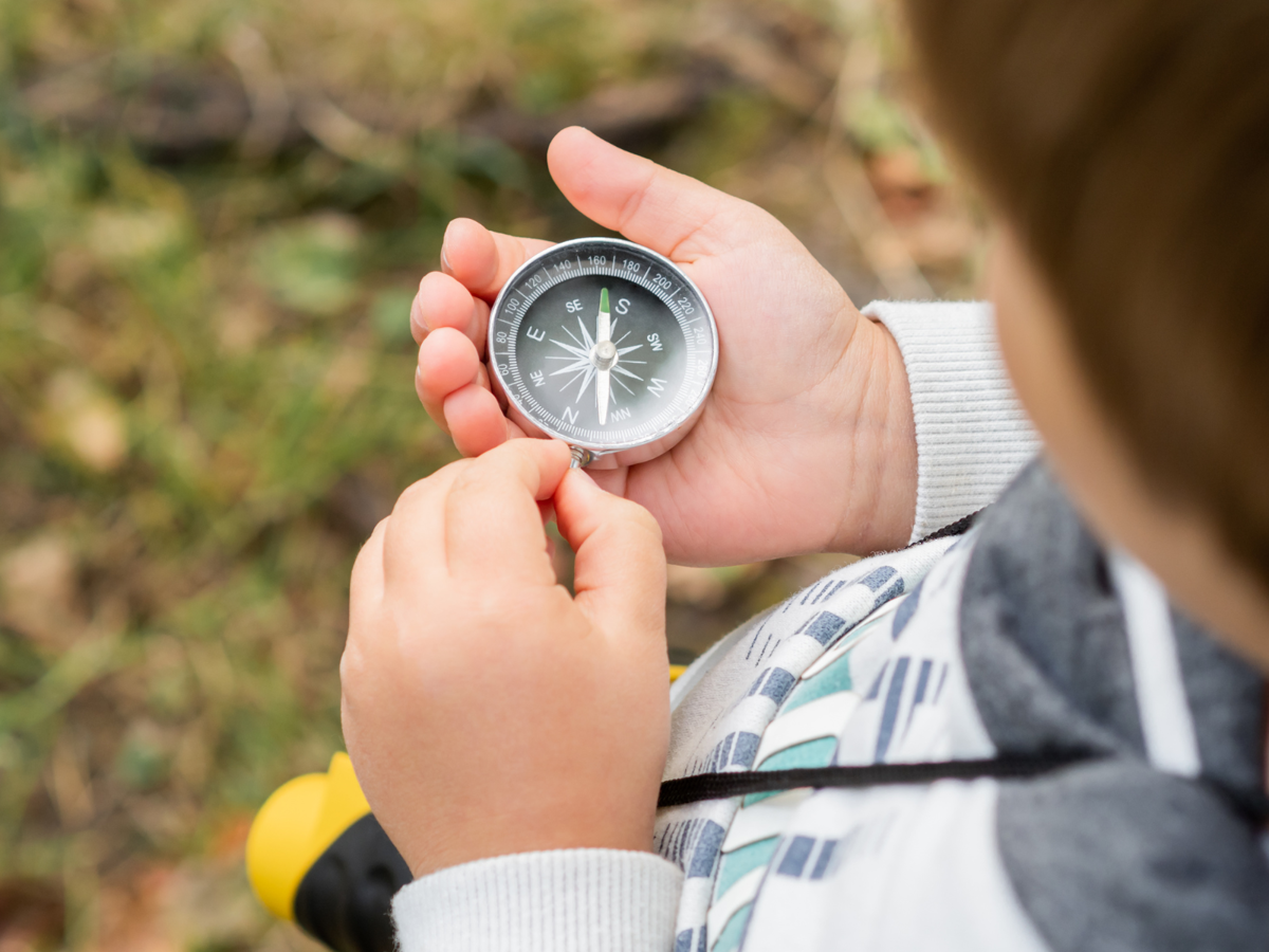 A young child is look at a metal compass that they are holding in their hand.