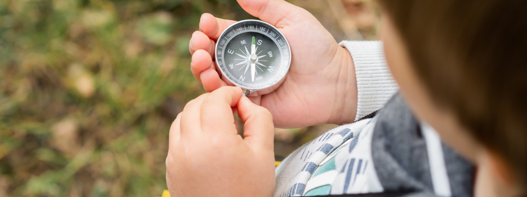 A young child is look at a metal compass that they are holding in their hand.