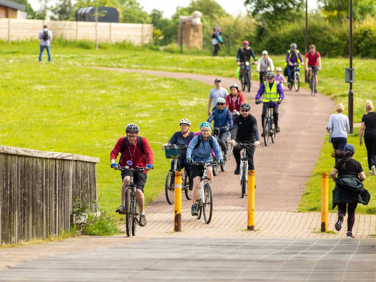 Group of people on a bike ride at Furzton Lake, coming down the hill over bridge