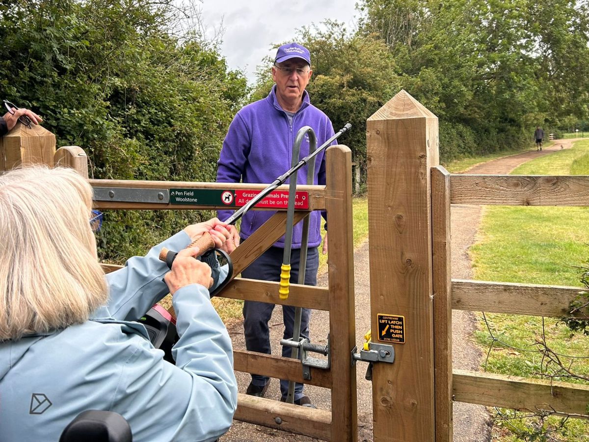 Person on mobility scooter holding out stick in front of gate