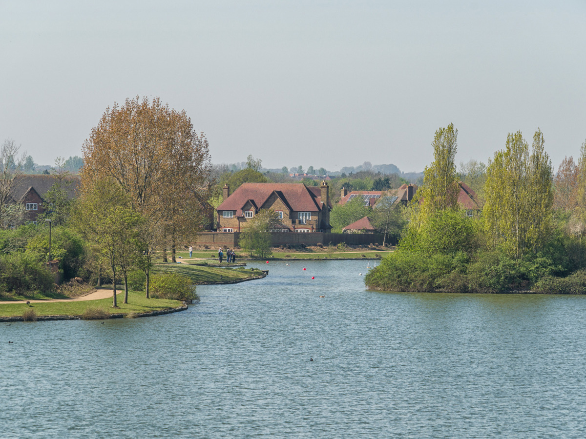 View across lake with water in foreground and houses in background.