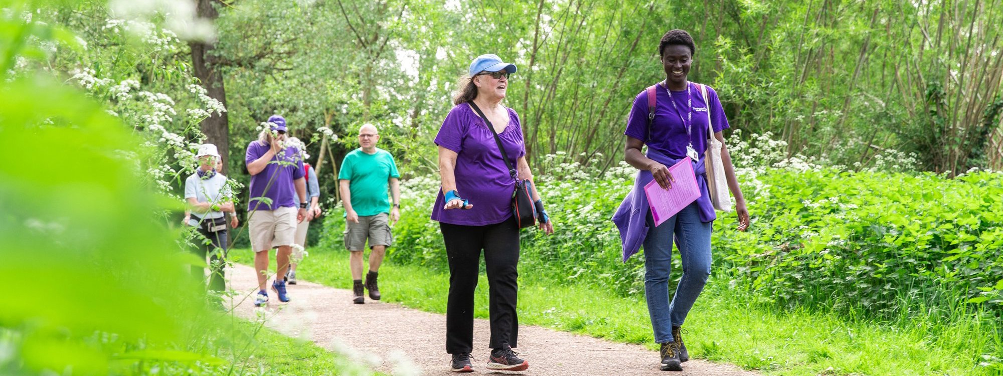 People walking along path in a park with staff in purple Parks Trust uniform