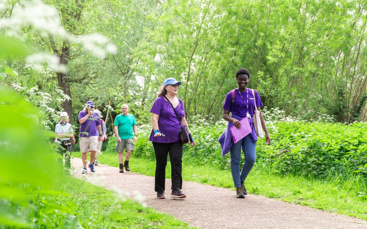 People walking along path in a park with staff in purple Parks Trust uniform