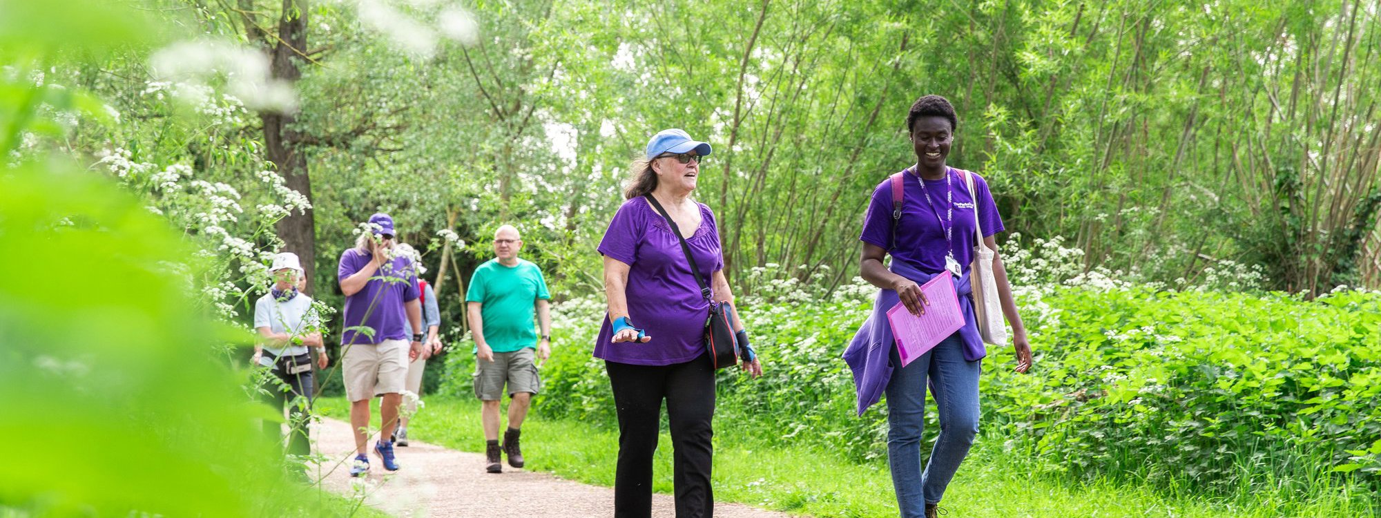 People walking along path in a park with staff in purple Parks Trust uniform