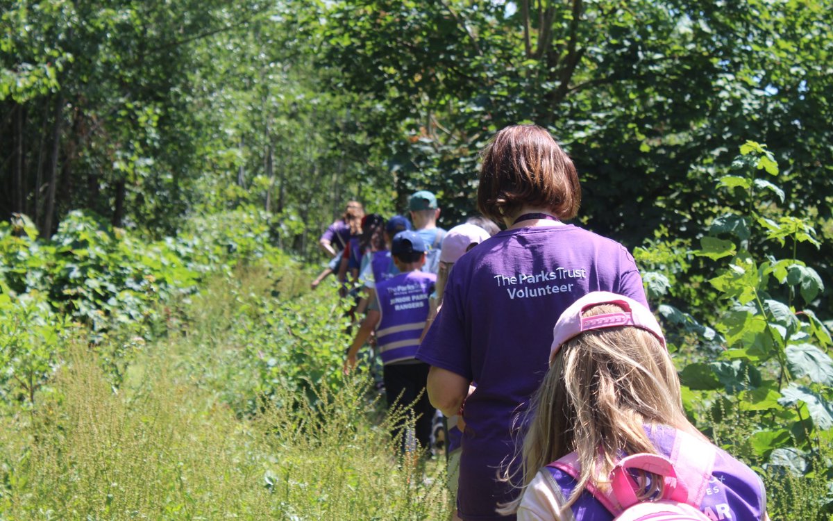 Volunteer in purple t'shirt walking through park with children