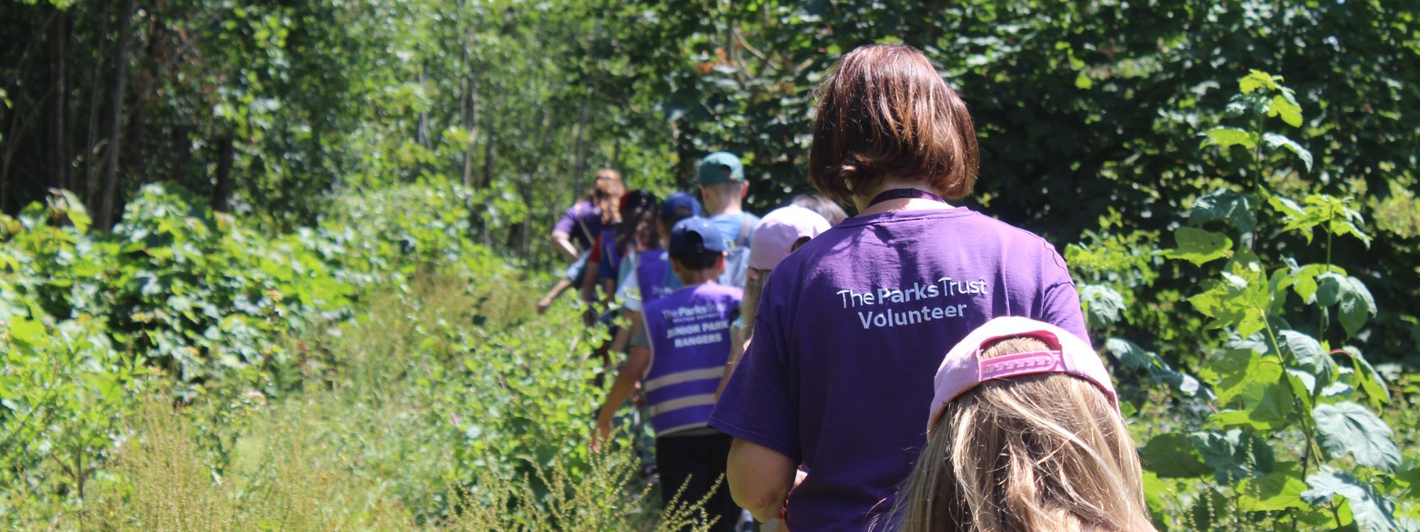 Volunteer in purple t'shirt walking through park with children
