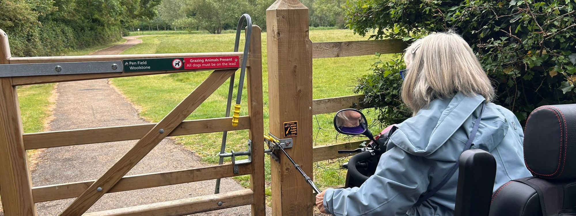 Person on mobility scooter opening gate with stick