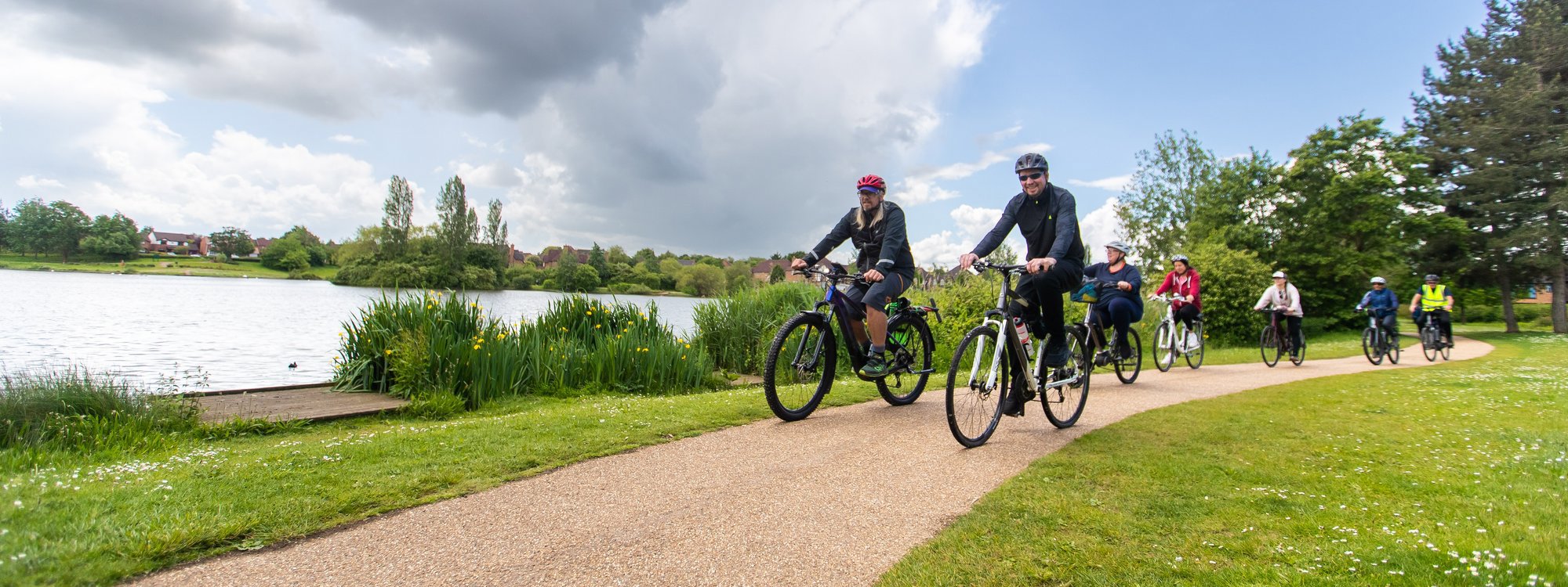 2 cyclists next to a lake with a beautiful sky overhead