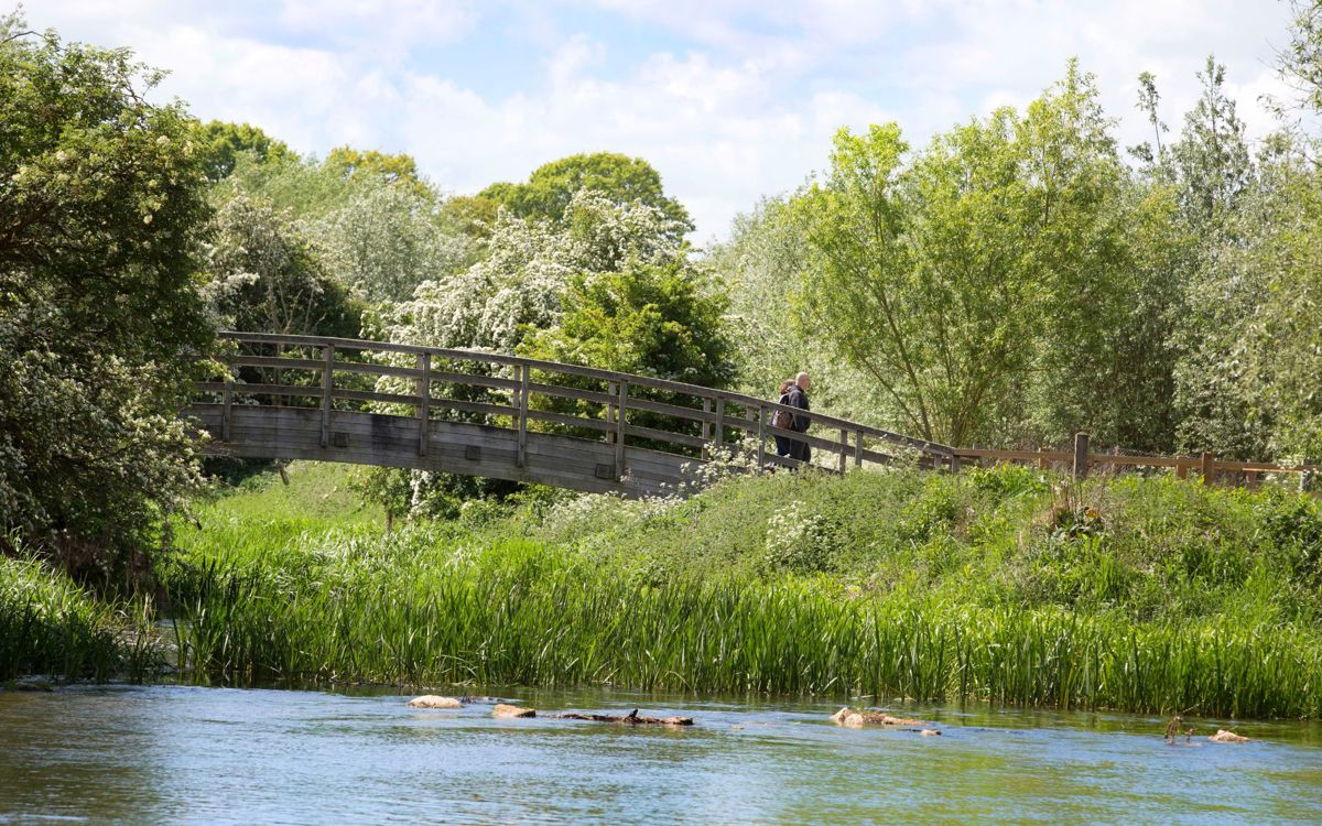 People crossing wooden bridge across river