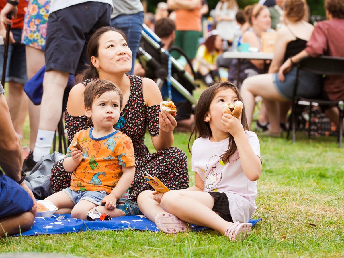 A young family sat on a picnic blanket enjoying some snacks