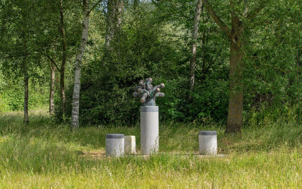 Art sculpture made on pedestal with stools around surrounded by long grass
