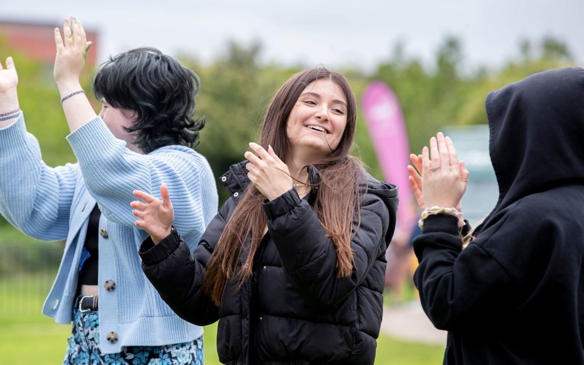 three teenagers smiling and clapping at an event 