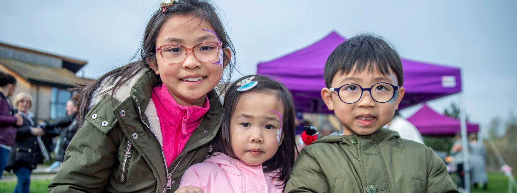 Three children at an outdoor event smiling at the camera
