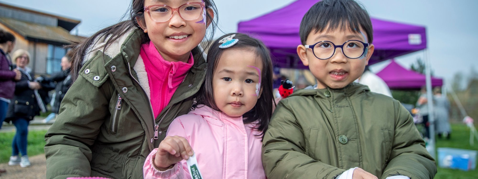 Three children at an outdoor event smiling at the camera