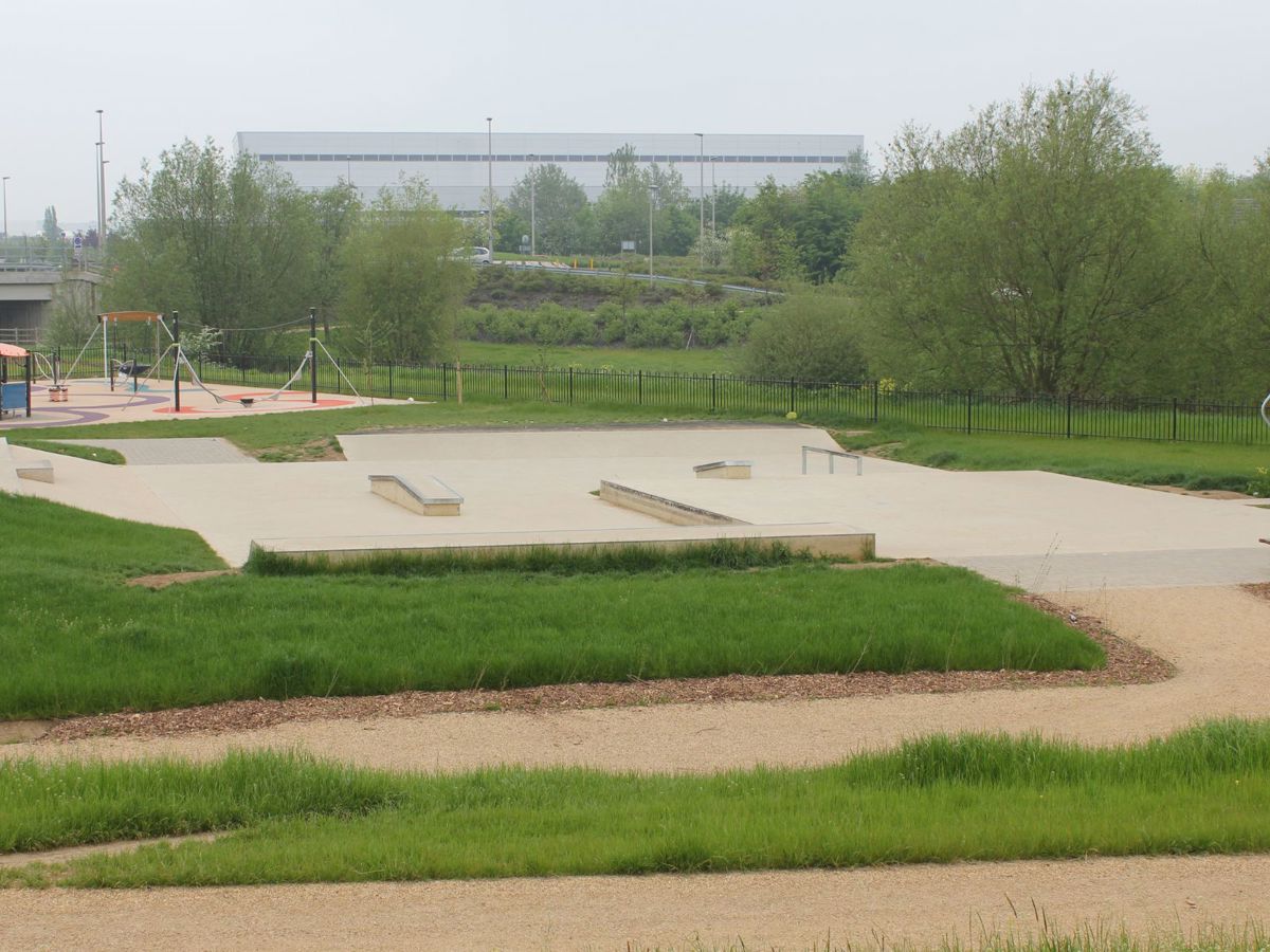 Skate park surrounded by grass and green trees on a cloudy day