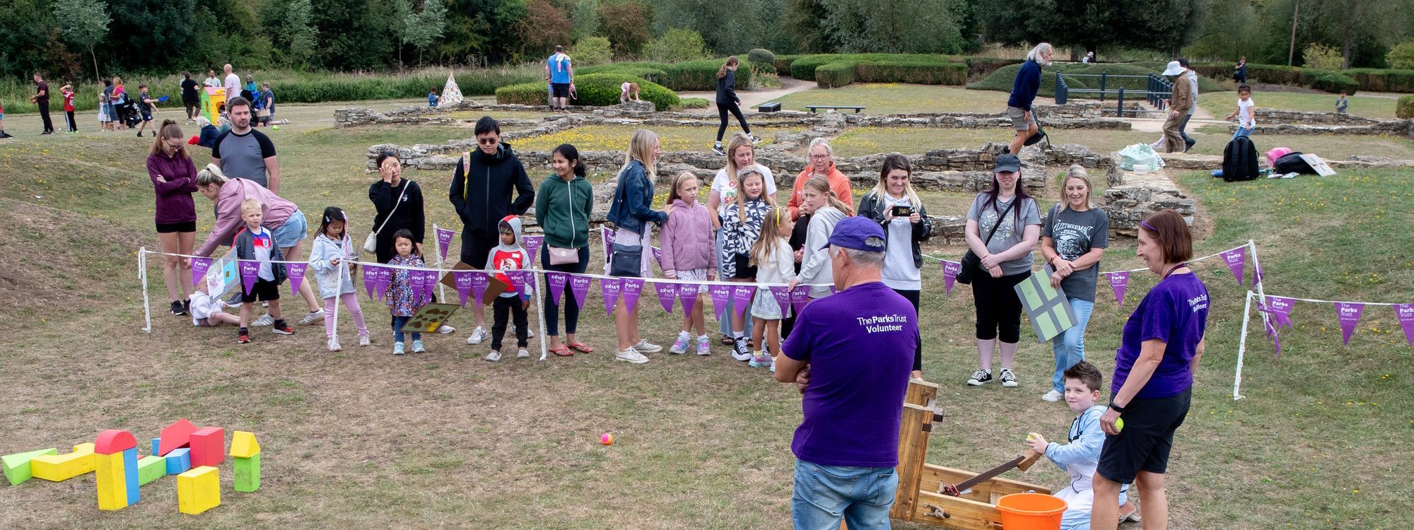 Volunteers running an activity in front of the Roman Villa site, where children can use a roman catapult model to knock foam bricks over.