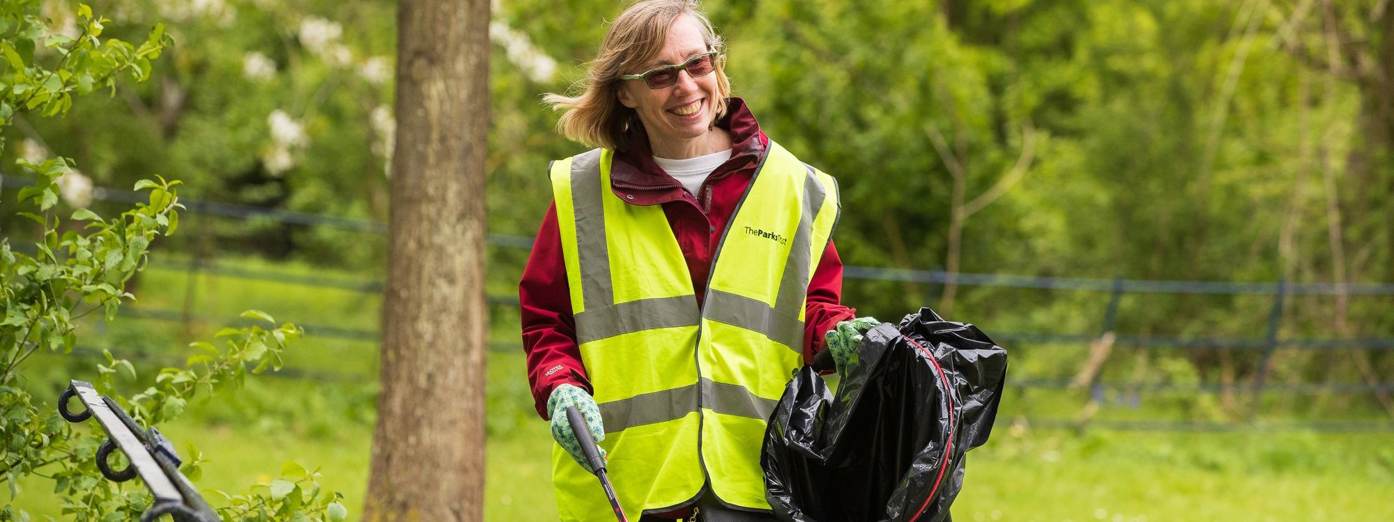 A solo female volunteer in hivis litter picking in a parkland scene