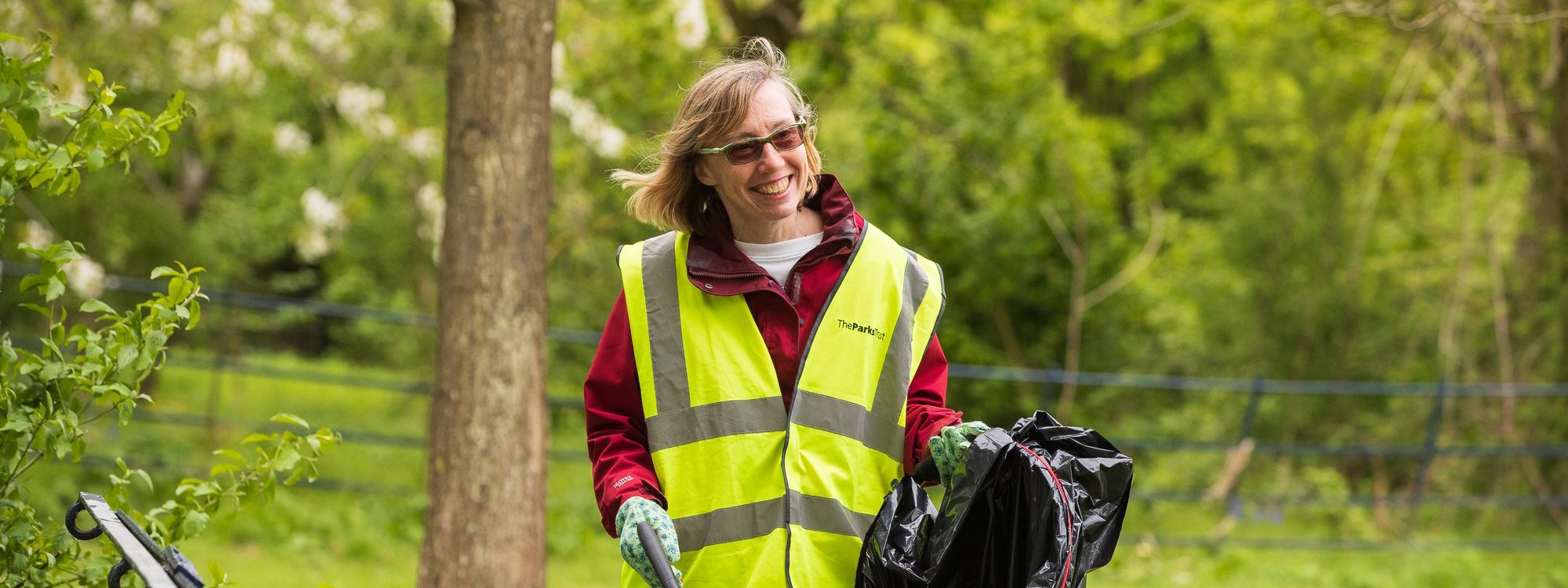 A solo female volunteer in hivis litter picking in a parkland scene