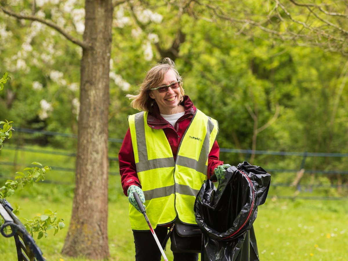 A solo female volunteer in hivis litter picking in a parkland scene