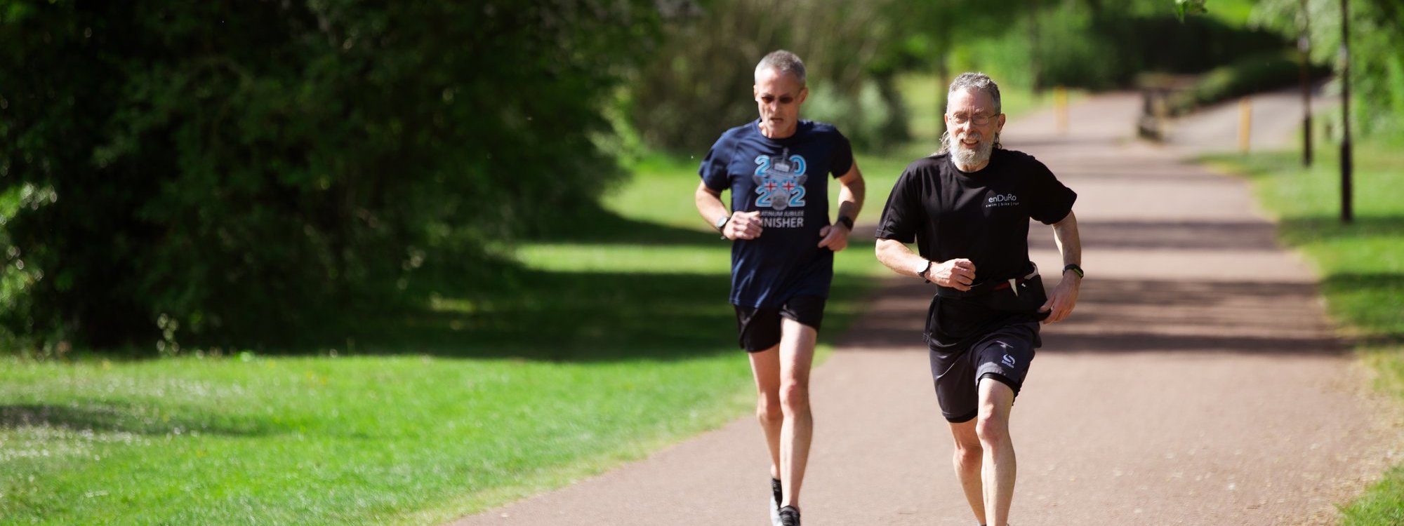 Two male runners striding along a Redway in parkland 