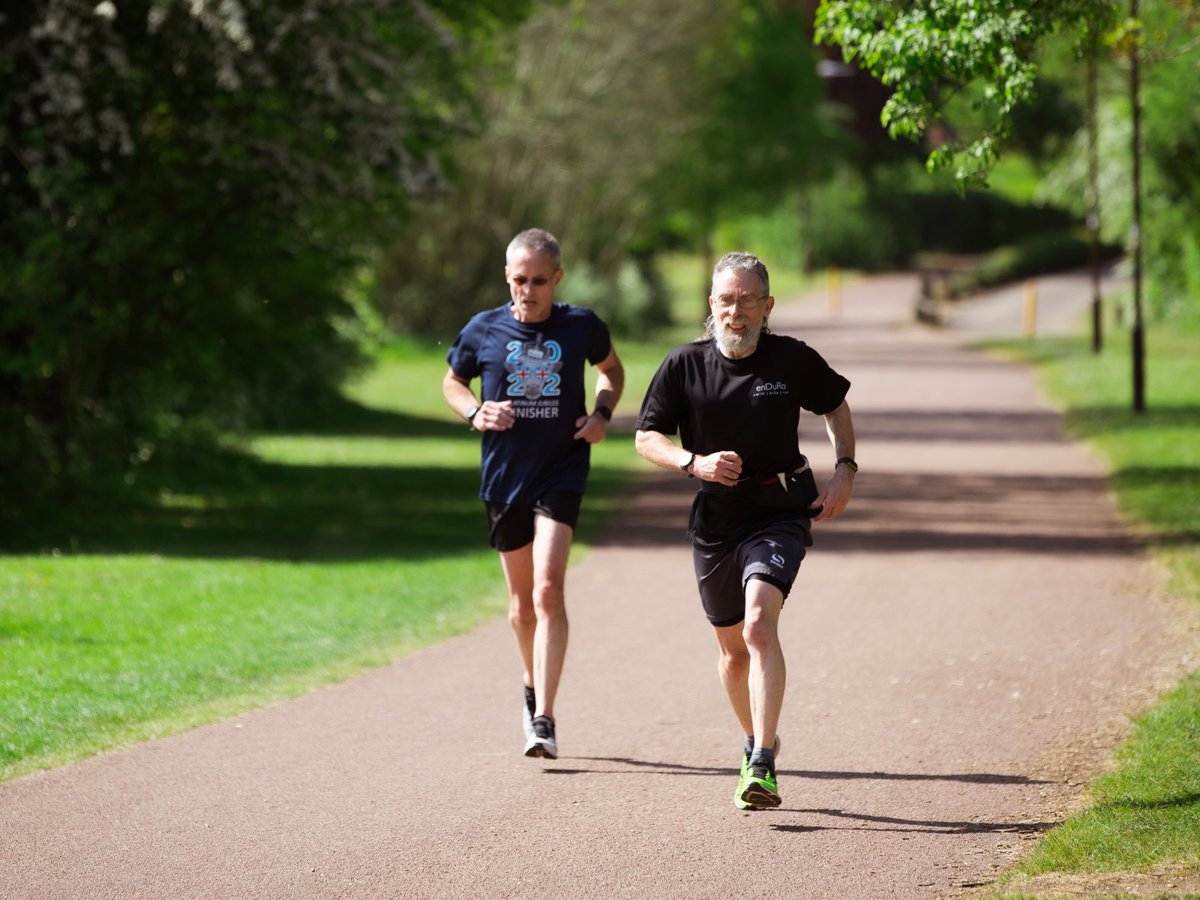 Two male runners striding along a Redway in parkland 