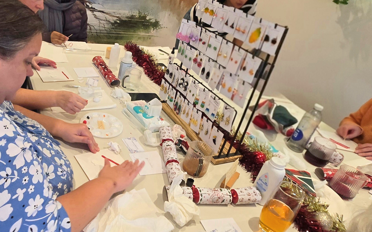 Several people sit around a table, viewing and trying different jewellery and beauty products.