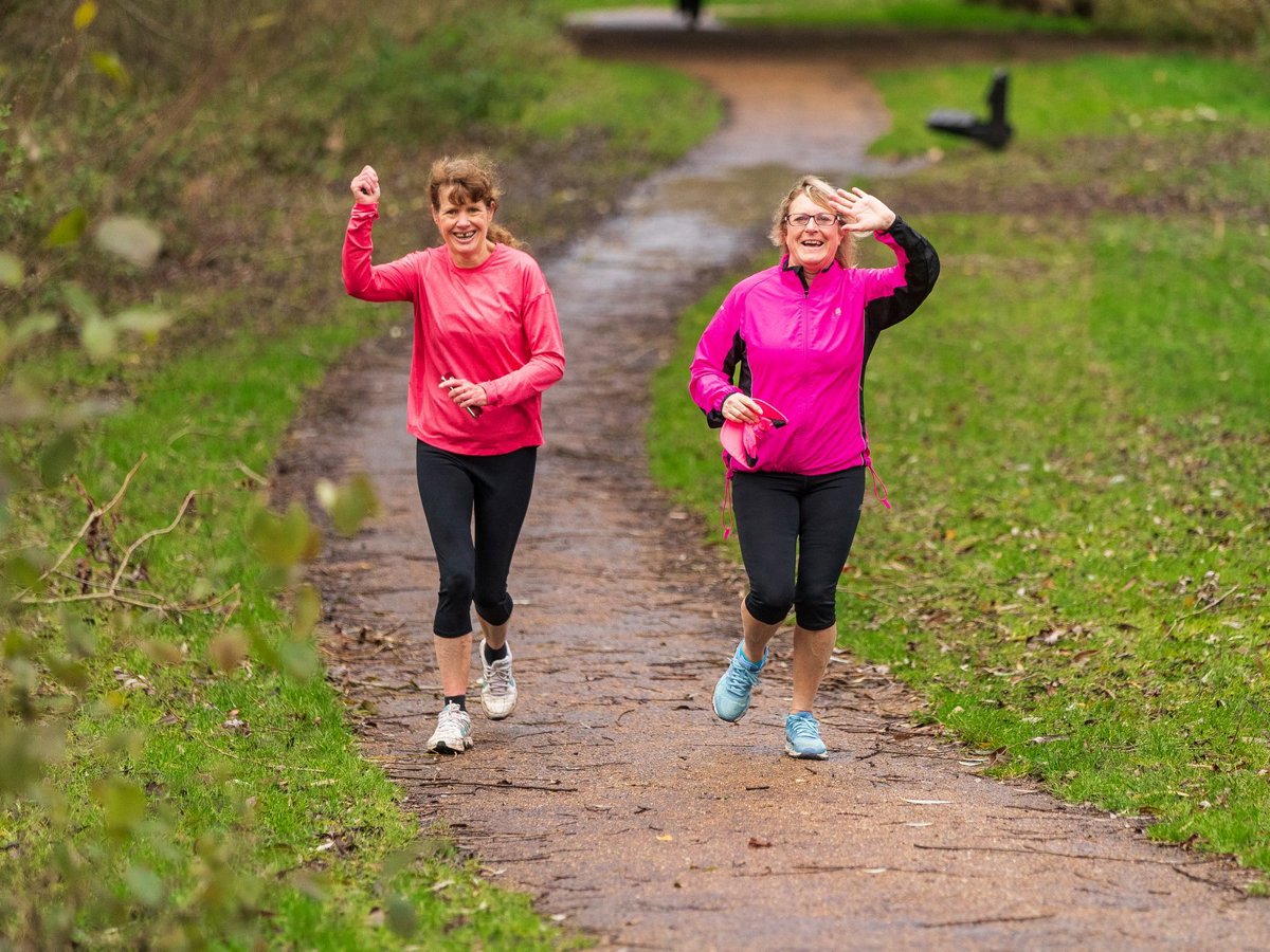 Two female runners waving and smiling in green parkland