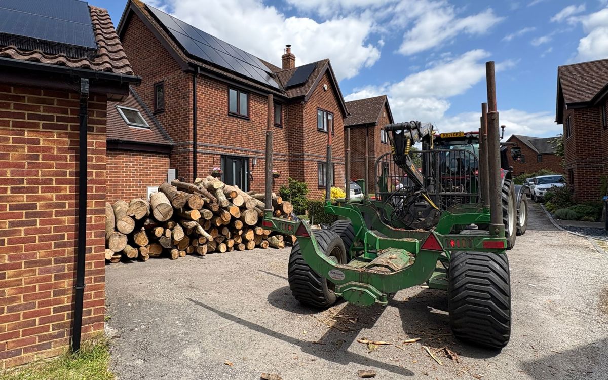 Tractor delivering timber on driveway outside house