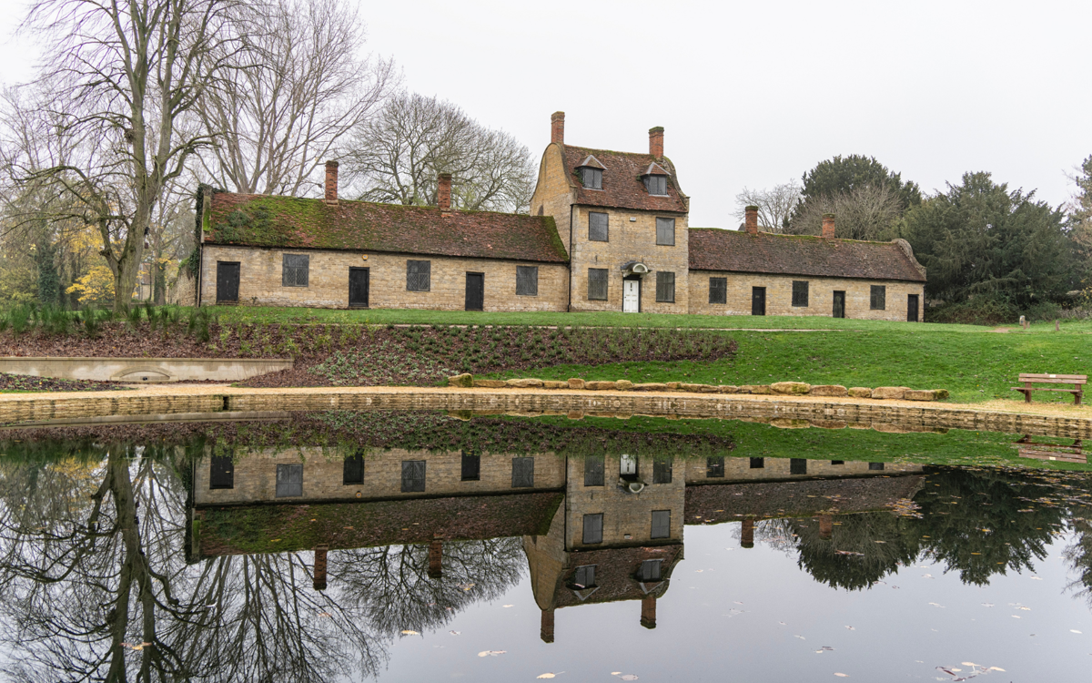 An old school building known as the Alms Houses. Its reflection is in the pond in below it.