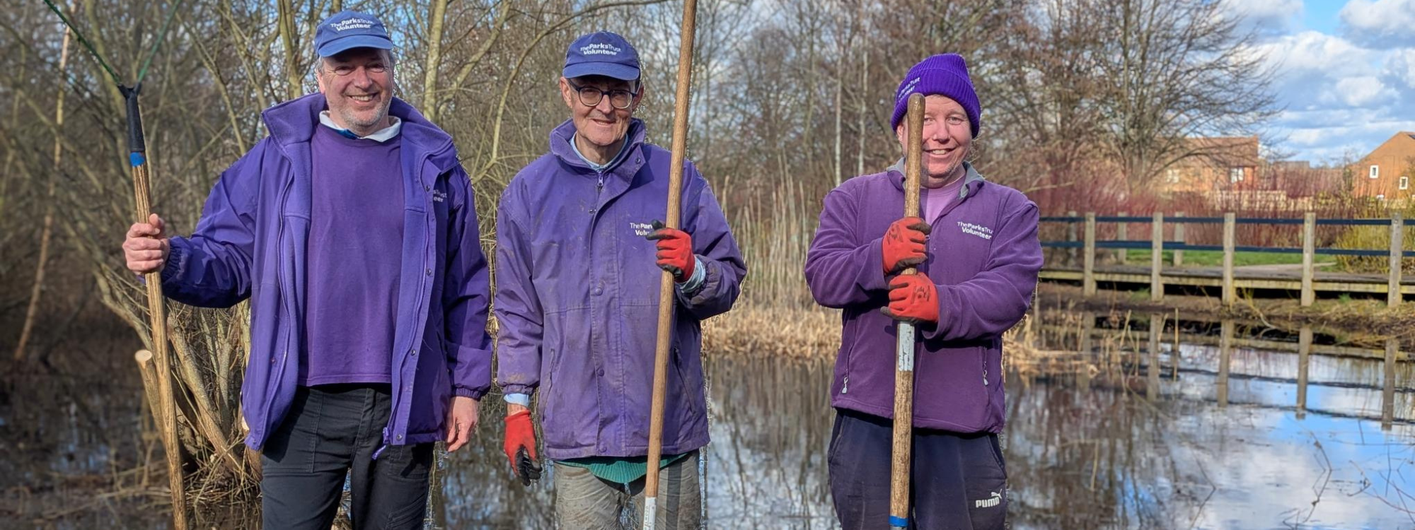 Three Parks Trust volunteers in purple uniform holding shovels